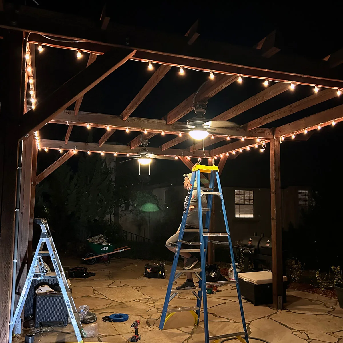 Electrician installing outdoor patio lighting in Sacramento at night under wooden pergola
